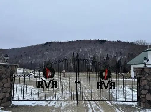 Gated entrance to RiverVail Ranch with "RVR" logo and holiday wreaths, surrounded by snow-covered landscape and mountains in the background.