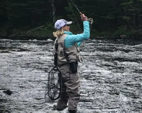Woman fly fishing in Clear Stream at RiverVail Ranch, wearing fishing gear and casting line in a natural setting.