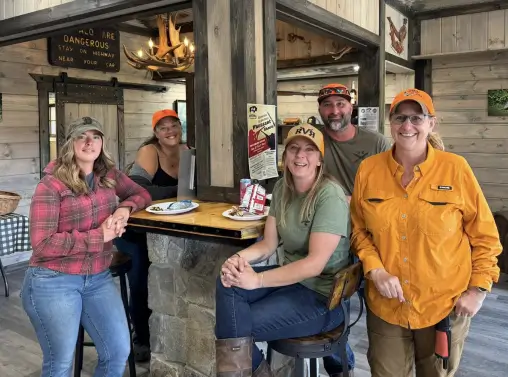 Group of five smiling individuals in outdoor gear at RiverVail Ranch's Roost Clubhouse, enjoying a meal and showcasing a friendly atmosphere.