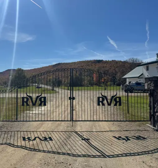 Gated entrance to RiverVail Ranch with "RVR" logo, surrounded by scenic hills and blue sky, inviting guests to outdoor recreation.