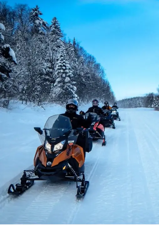 Group of snowmobilers riding on a snowy trail surrounded by winter trees, showcasing outdoor adventure activities available at RiverVail Ranch retreats.