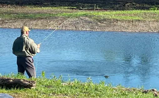 Man fishing in a tranquil pond at RiverVail Ranch, surrounded by greenery, showcasing outdoor recreation opportunities for members.