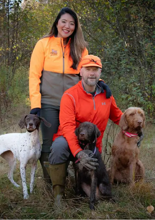 Couple in bright outdoor attire with three dogs in a natural setting, emphasizing outdoor activities and safety during hunting season at RiverVail Ranch.